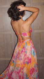 Close-up back view showing the crossed tie straps, open waist cutout and pleated floral skirt of the maxi dress