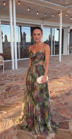 Model in the green floral maxi dress with cutout waist, V neckline and thin straps, holding a woven clutch on a stone terrace