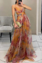 Side view of a flowing multicolour maxi dress with pleated skirt and spaghetti straps, paired with a metallic clutch