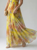 Close-up of the flowing pleated skirt in yellow and orange watercolour print, paired with strappy gold heels