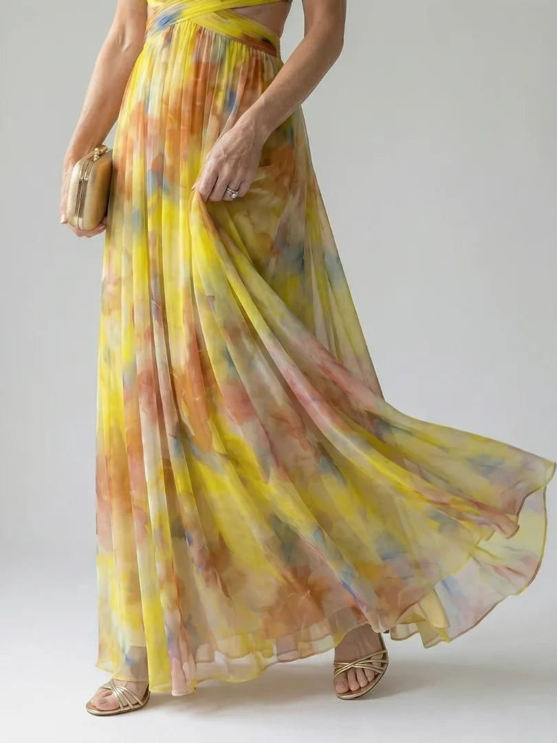 Close-up of the flowing pleated skirt in yellow and orange watercolour print, paired with strappy gold heels