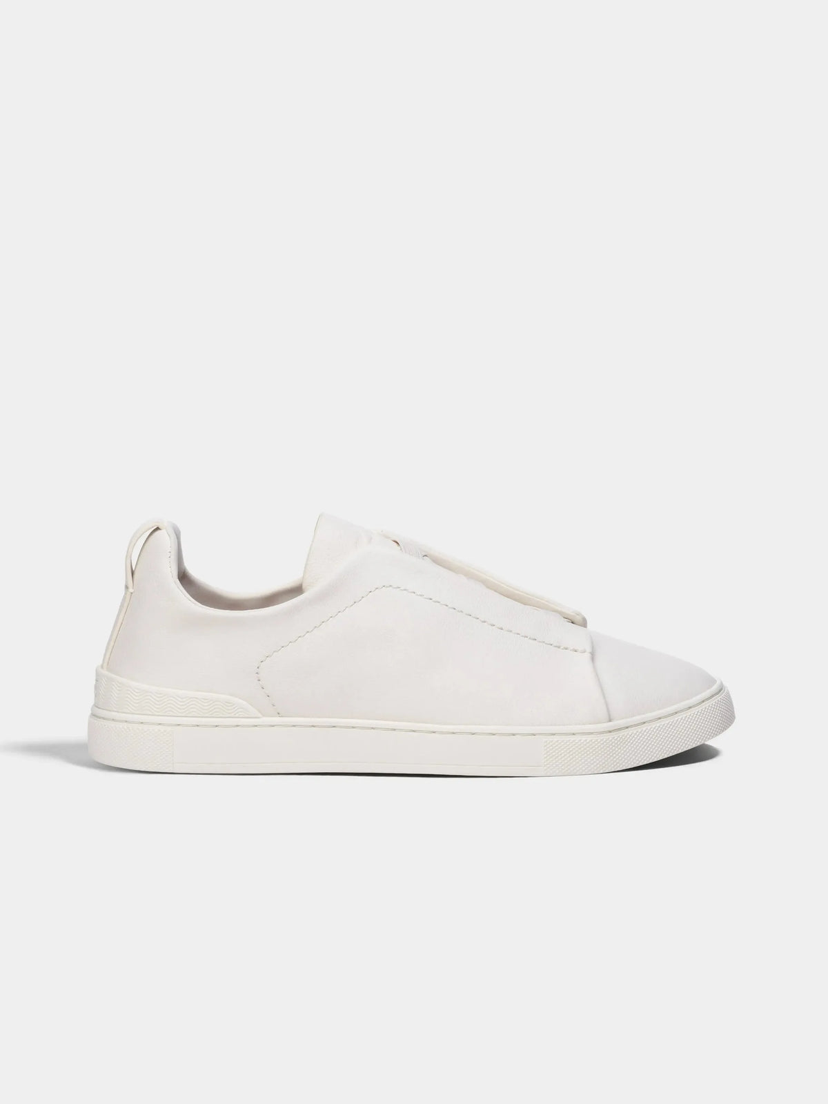 Side profile of a white leather low-top sneaker with elastic laced vamp and ridged white rubber sole.