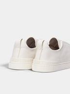Close-up back view of two white leather sneakers showing heel pull tabs, stitching detail and textured outsole.