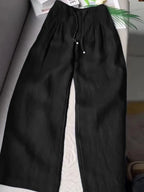 Black wide-leg pants with pintuck waistband and drawstring tie, laid flat on a couch