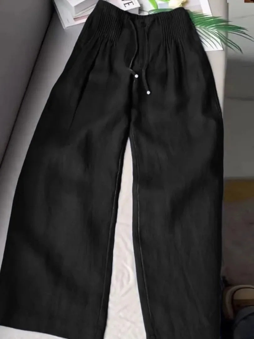 Black wide-leg pants with pintuck waistband and drawstring tie, laid flat on a couch