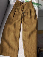 Khaki gold wide-leg pants with pintuck waistband and drawstring, laid flat on a couch
