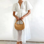 White windowpane-check midi dress with puff sleeves and a fitted button-front waist, worn with a woven top-handle bag.