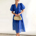 Royal blue windowpane-check puff-sleeve midi dress with button-front bodice, paired with a straw clutch bag.