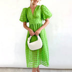 Bright green windowpane-check midi dress with puff sleeves and button-front detailing, worn with a white woven bag.