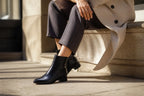 Close-up of a black leather ankle boot worn with dark trousers, showing the low block heel