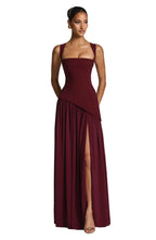 Front view of model in a burgundy sleeveless maxi dress with squared neckline, fitted bodice and high leg slit