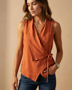 Model wearing a burnt orange wrap-front sleeveless top with draped V neckline and a slim waist tie.